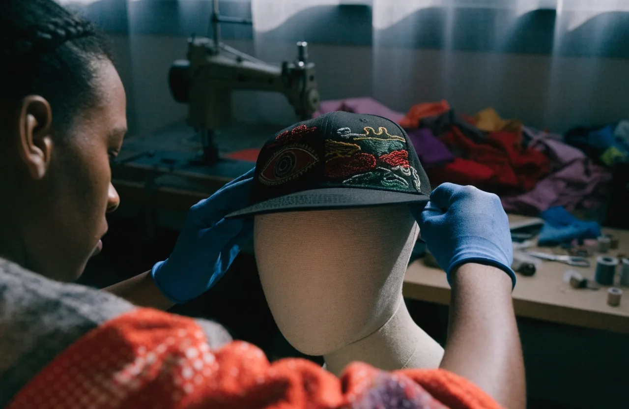 Gorra negra bordada apoyada sobre papeles de molde en la mesa de taller